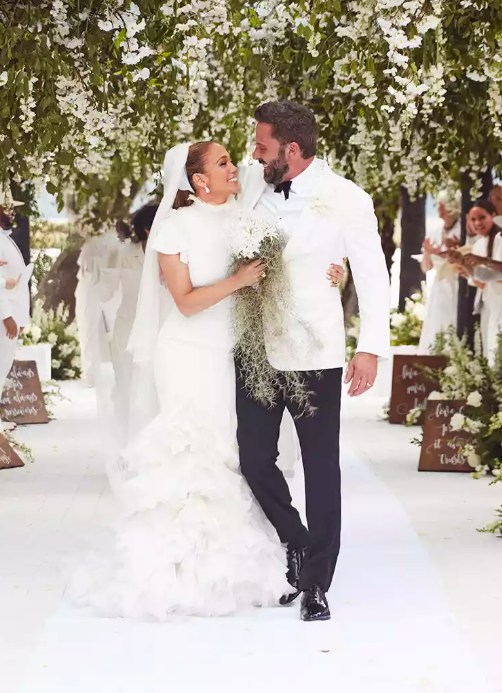 Jennifer Lopez in her wedding dress walking down the aisle smiling and looking at Ben Affleck in his suit
