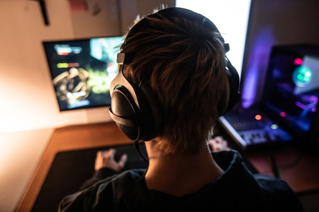 Rear View of Gamer with Headset on Playing Online Video Games in Dark Room - stock photo