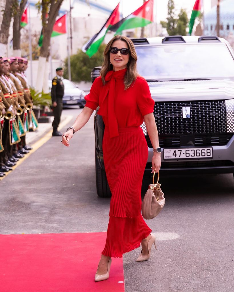 Queen Rania arriving at parliament in red blouse and skirt