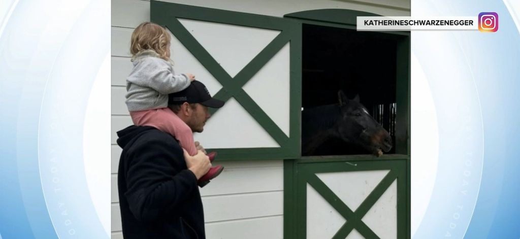 photo of chris pratt with daughter on his shoulders standing by horse barn with black horse