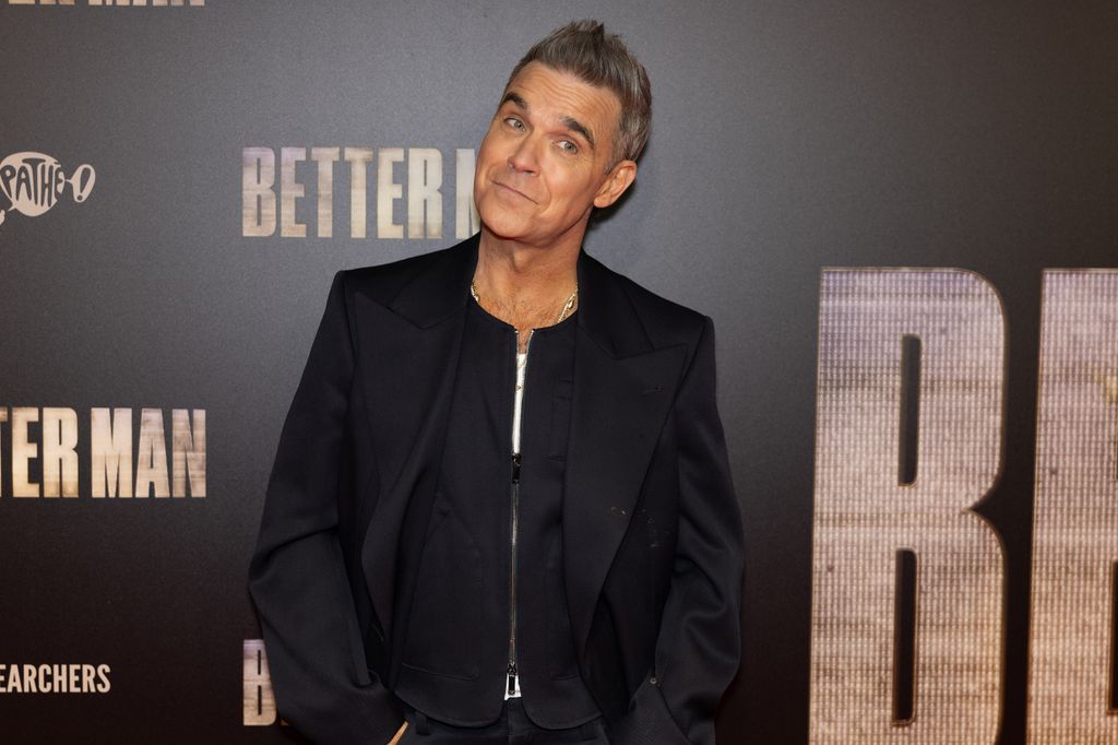 Robbie Williams smirking in a black suit from the Better Man premiere 