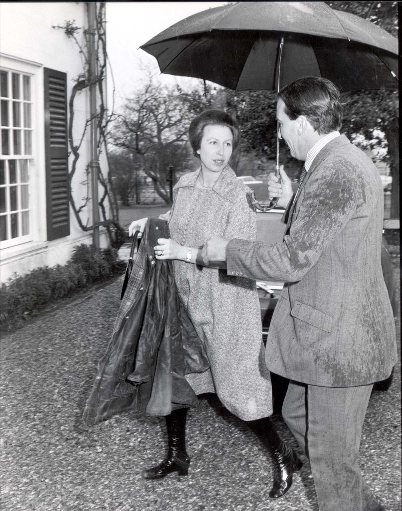 Princess Anne in knee-high boots under an umbrella