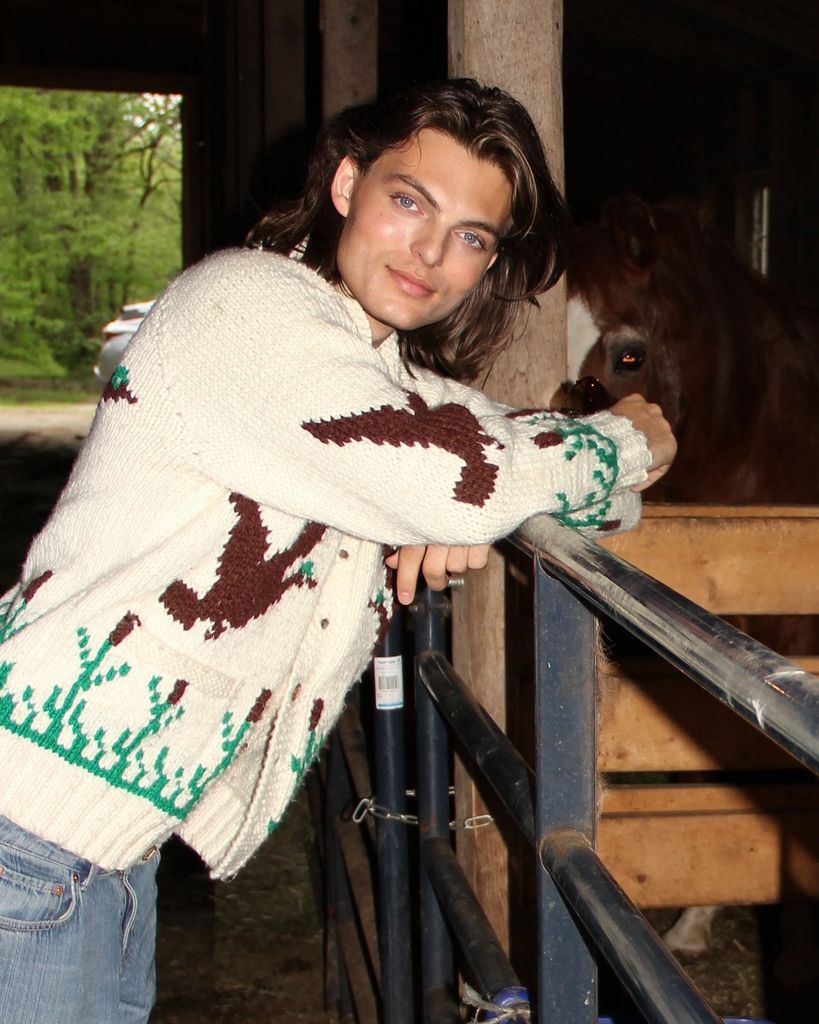 A photo of Damian Hurley wearing a cream cardigan and posing with a horse