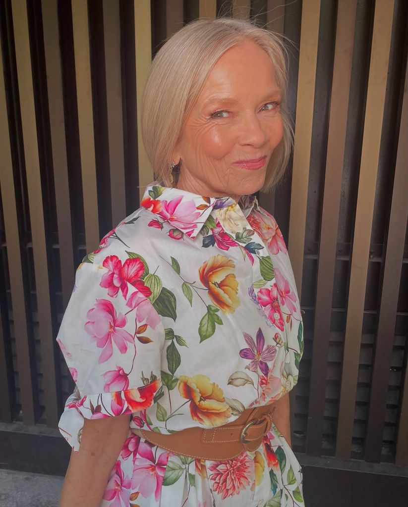 Femme plus âgée en robe florale souriant légèrement avec du rouge à lèvres rose 