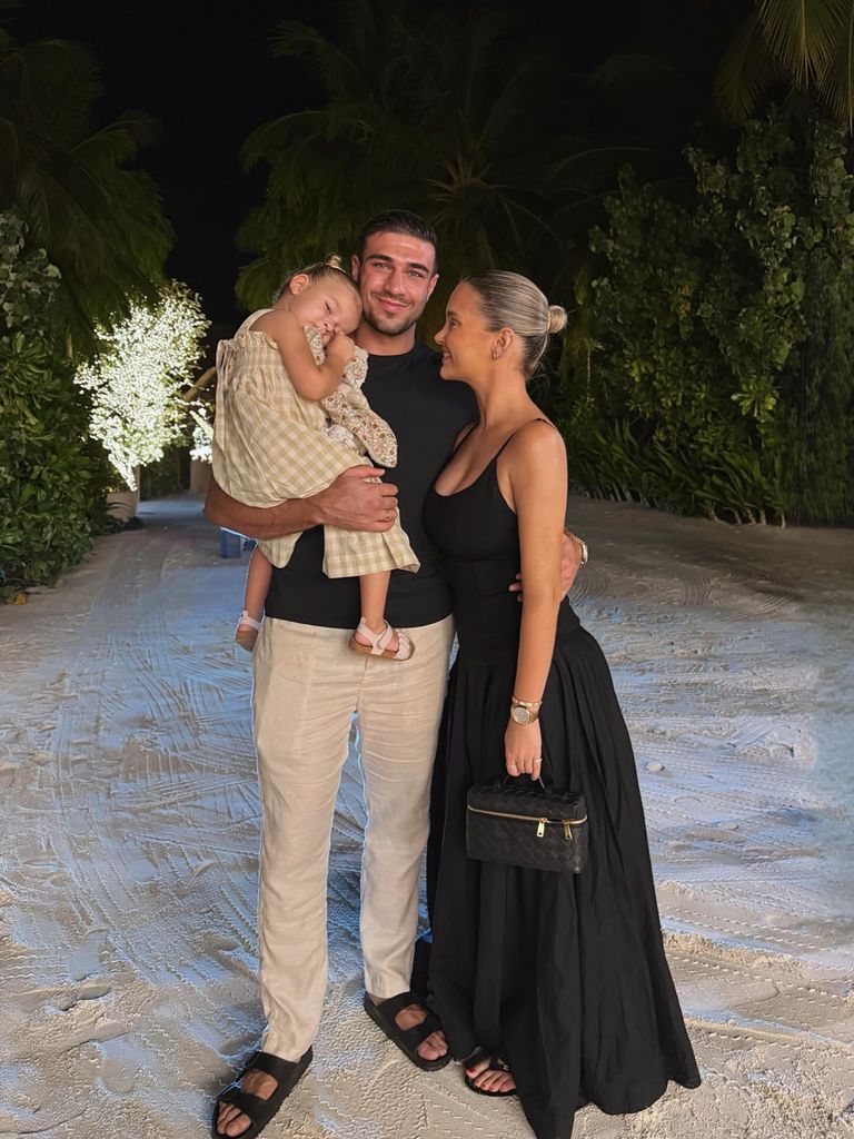 Molly-Mae Hague poses on a beach with Tommy Fury who carries their baby Bambi