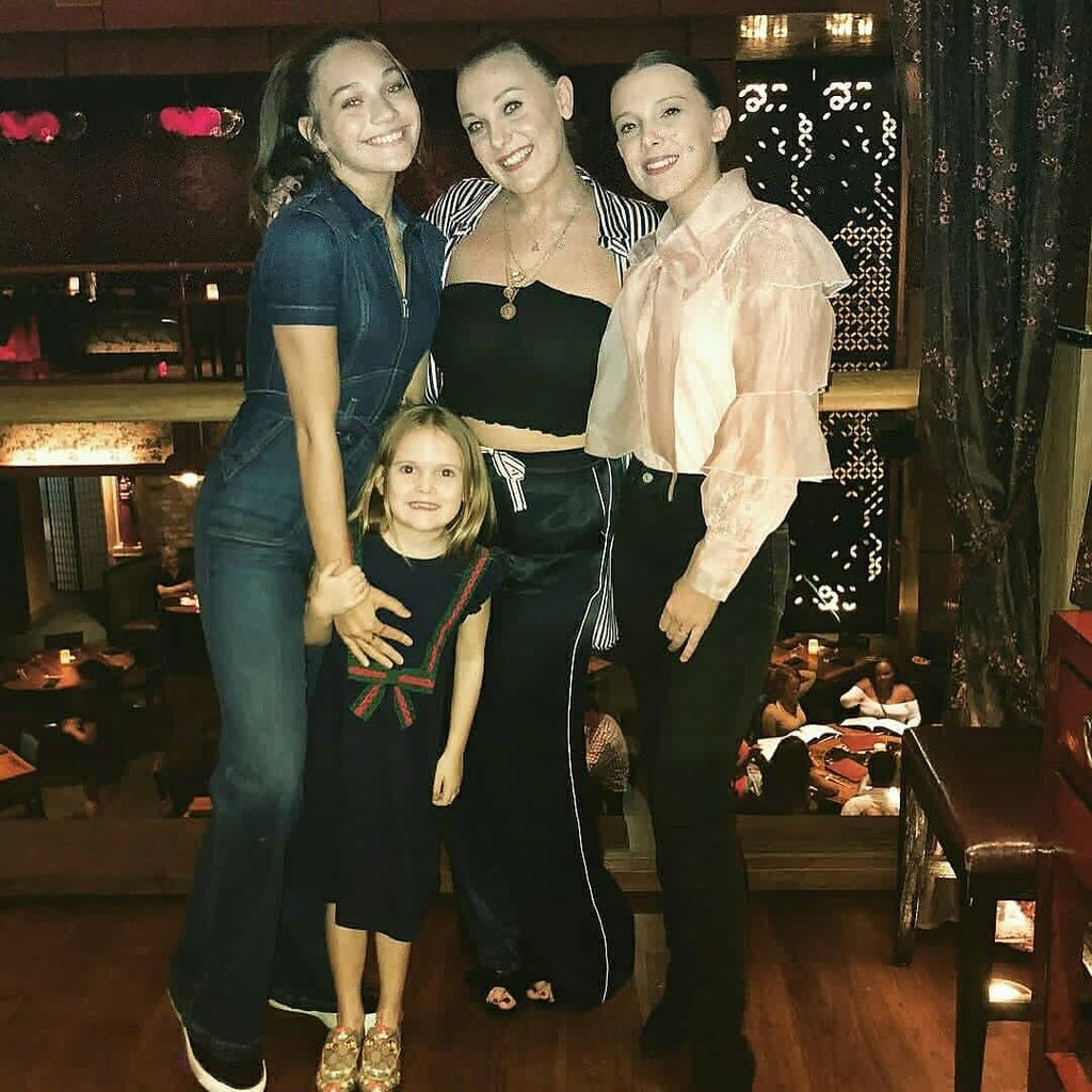 Millie Bobby Brown with her sisters and mother in a dark party setting 