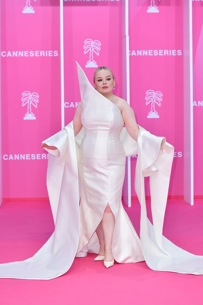 Nicola Coughlan on pink carpet in white dress with collar that sits up high next to her face