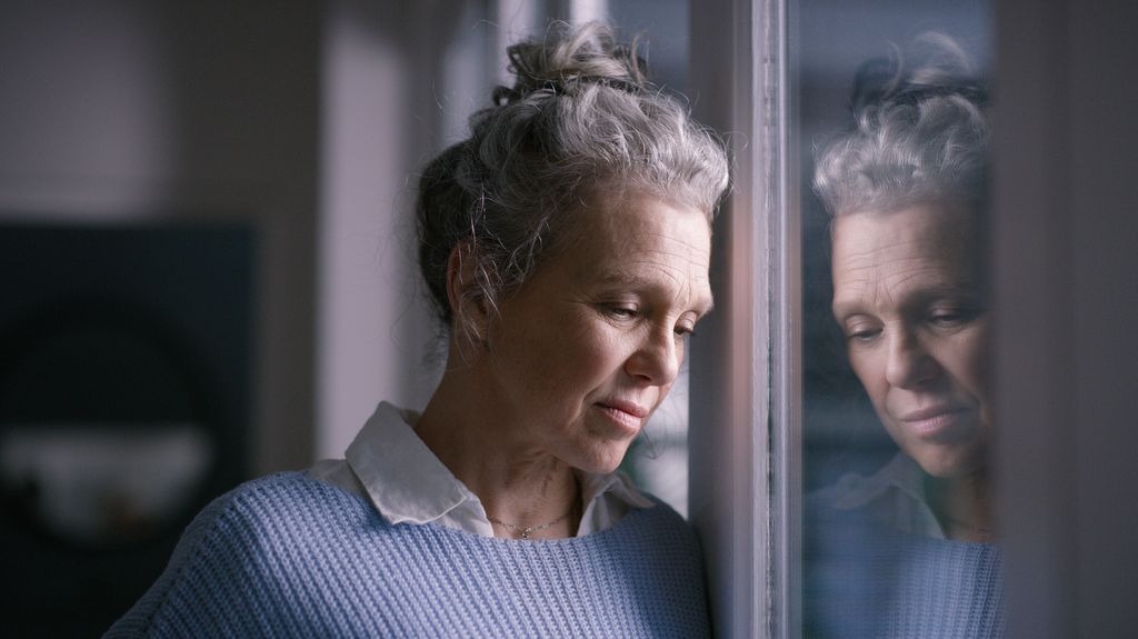 sad and senior woman by window looking, upset, lonely and unhappy in retirement home. Mental health, loneliness and and depressed elderly female thinking of problem, issues and crisis