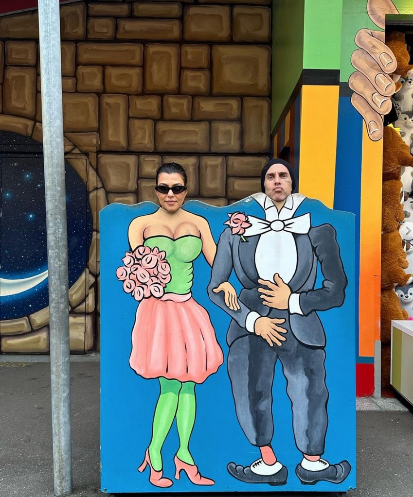 Photo shared by Travis Barker on Instagram March 2024 where he is posing with wife Kourtney Kardashian behind a wooden caricature.