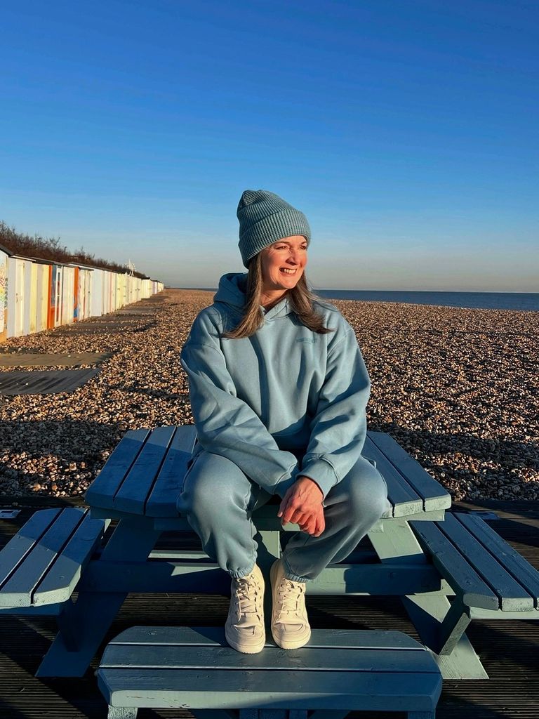 woman sitting in a tracksuit wearing a beanie hat at the beach