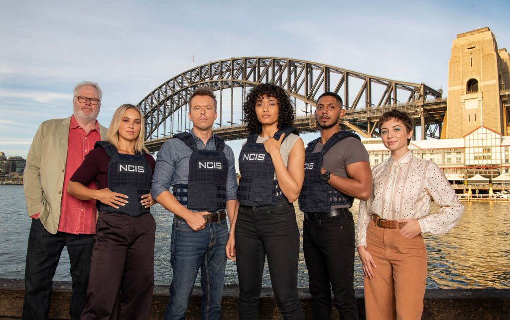 The NCIS:Sydney season 2 cast from left to right: William McInnes as Forensic Pathologist Dr. Roy Penrose, Tuuli Narkle as AFP Liaison Officer Constable Evie Cooper, Todd Lasance as AFP Liaison Officer Sergeant Jim \'JD\' Dempsey, Olivia Swann as NCIS Special Agent Captain Michelle Mackey, Sean Sagar as Special Agent DeShawn Jackson, and Mavournee Hazel as Forensic Pathologist Bluebird