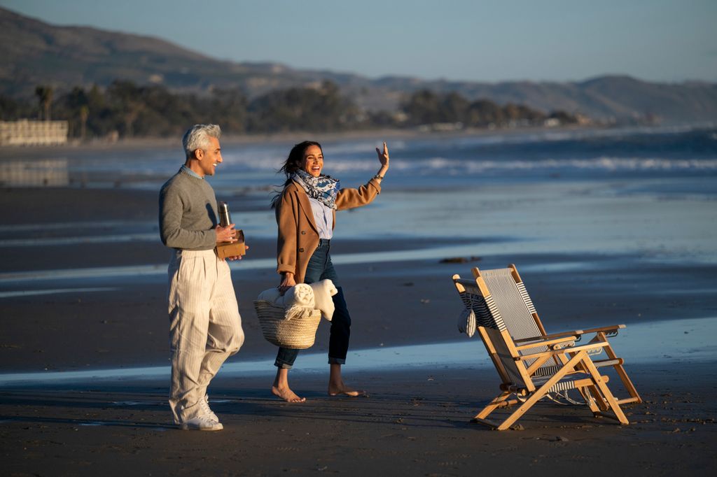 Meghan strolling barefoot on the beach with Tan France