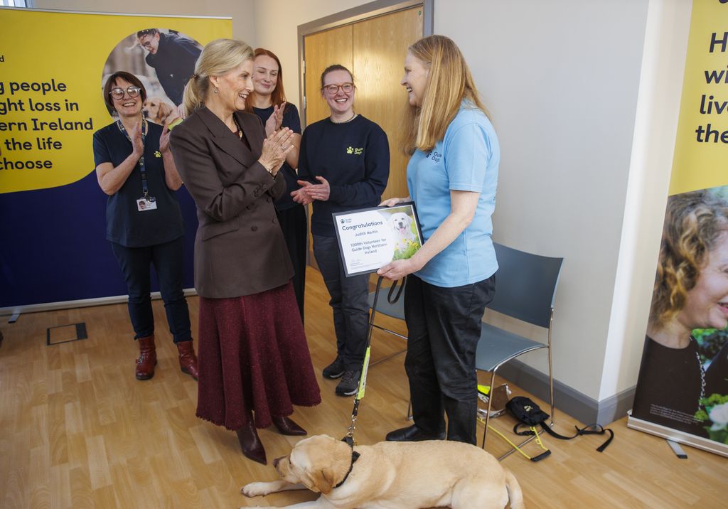 La duchesse d'Édimbourg (au centre à gauche) remet à Judith Martin (à droite) et à son chien-guide Brooke un certificat pour être le 1000e bénévole actif pour les chiens-guides d'Irlande du Nord.