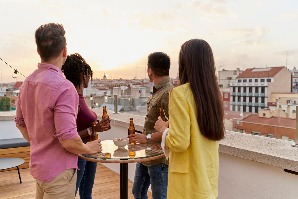 young friends standing in front of the table with bottles of beer in their hands looking up at the sky from the terrace