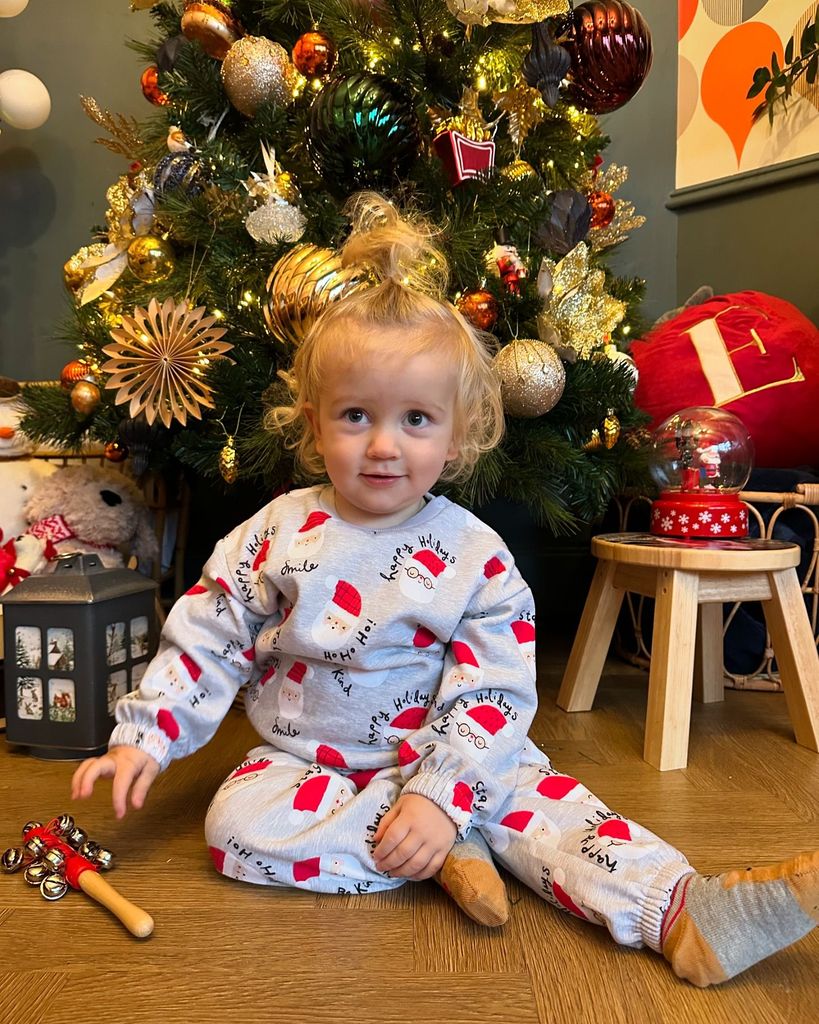 toddler sat in front of christmas tree in santa pyjamas