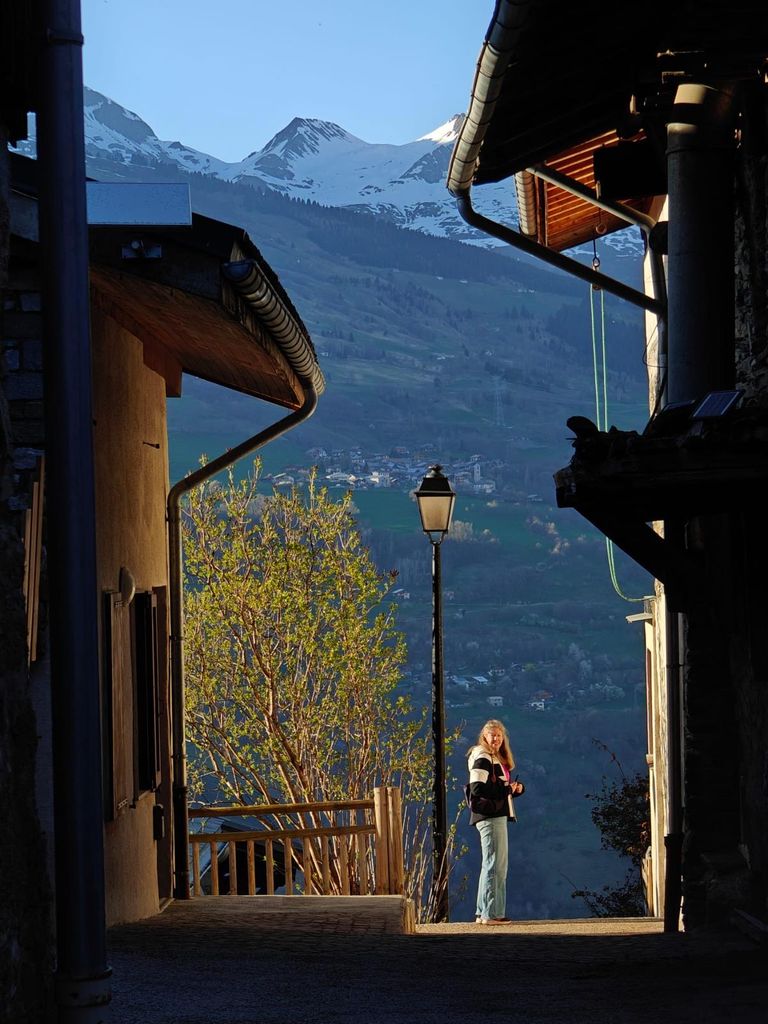 A woman standing in the sunlight inbetween houses