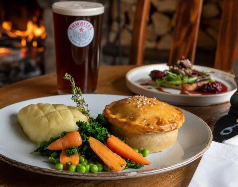 Pie, vegetables and mash on a plate next to a pint of ale