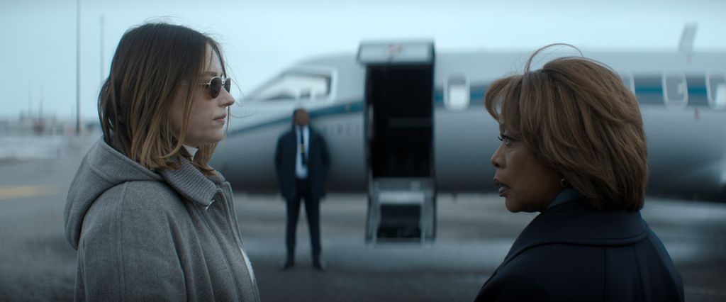 Two women stand in front of each other with a plane behind them