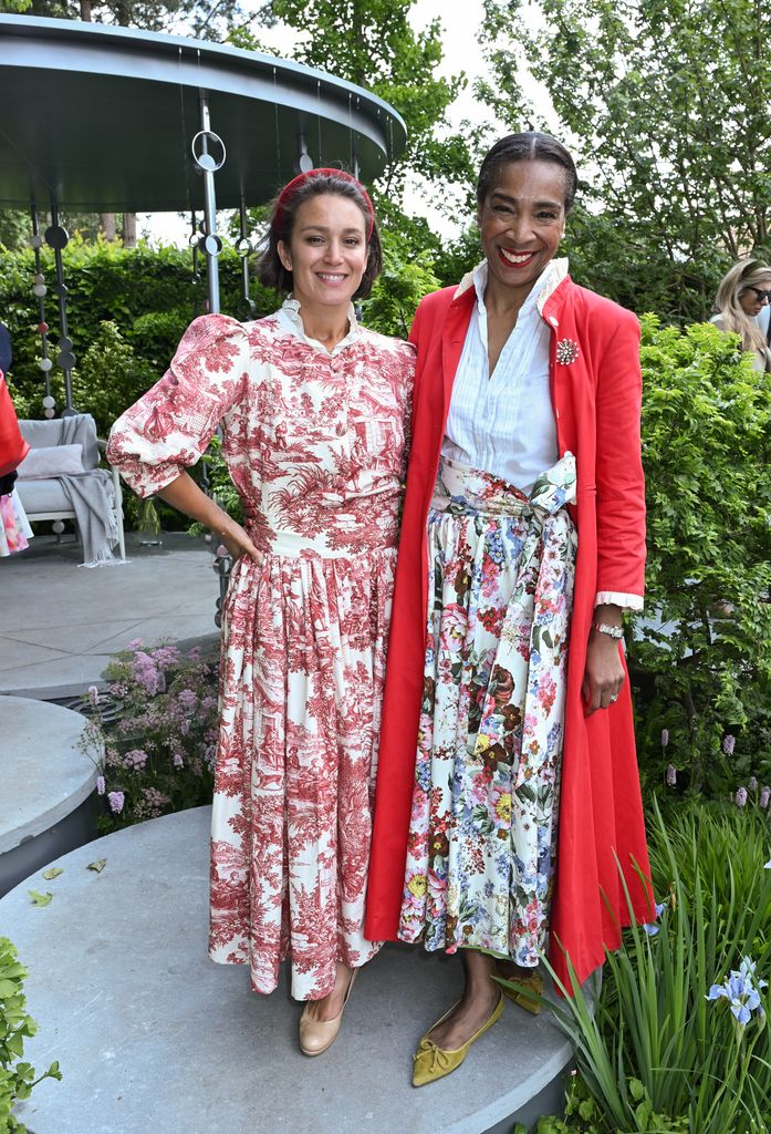 Leah Lane and Paula Sutton pose in matching red and floral-themed outfits featuring vintage prints, puff sleeves and a red coat at Chelsea Flower Show 2025.
