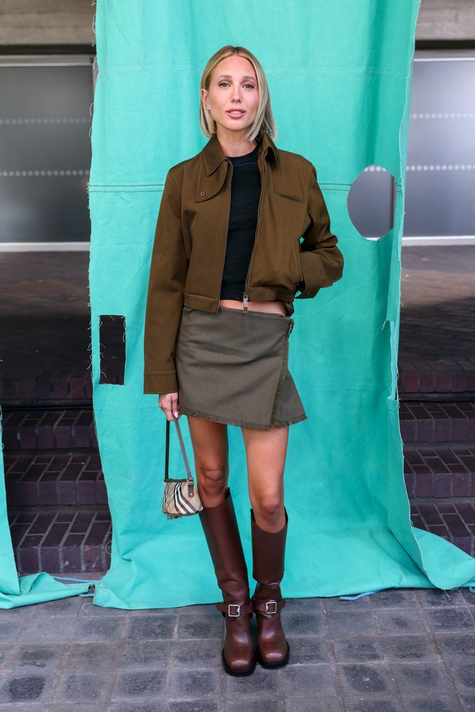 Princess Olympia wears a khaki cropped jacket, matching mini skirt, and brown knee-high boots with a mini Burberry bag at a fashion week show.