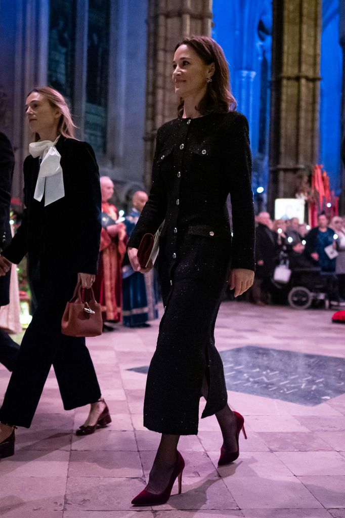 Pippa Middleton walks into Westminster Abbey in a glittering black Chanel-style tweed dress, featuring silver buttons and a slit. She pairs it with red velvet stiletto heels and a clutch.