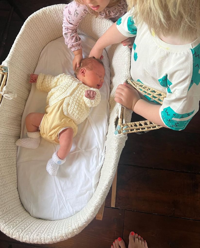 newborn baby in moses basket with kids around