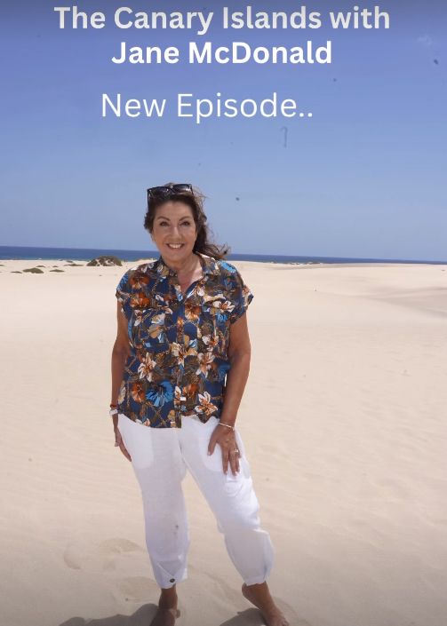 Jane McDonald on the beach in a floral shirt and white trousers