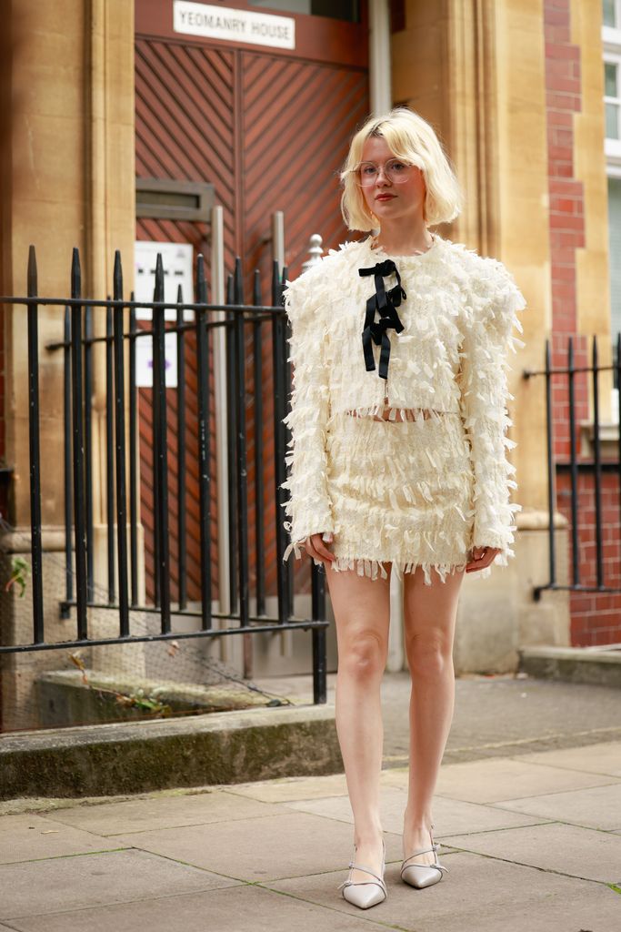 Maisie Peters wearing white Yuhan Wang bow tie cotton blend tweed jacket, bow tie tweed skirt and grey heels outside Yuhan Wang during London Fashion Week on September 20, 2025 in London, England.  (Photo by Hanna Lassen/Getty Images)