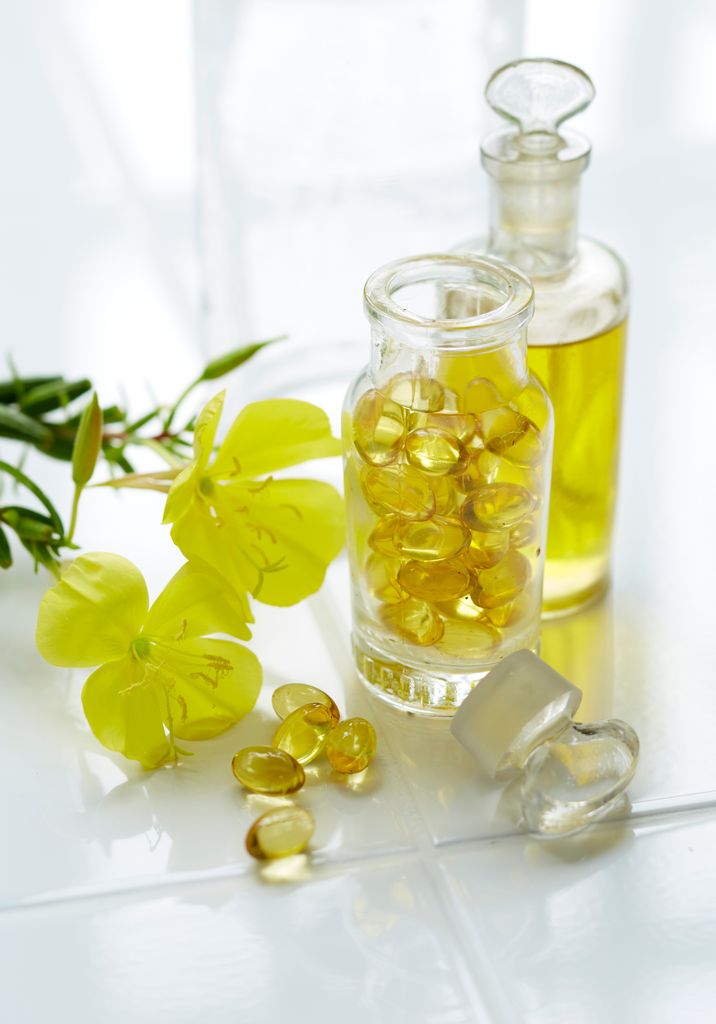Evening primrose oil, flowers and and capsules on white background