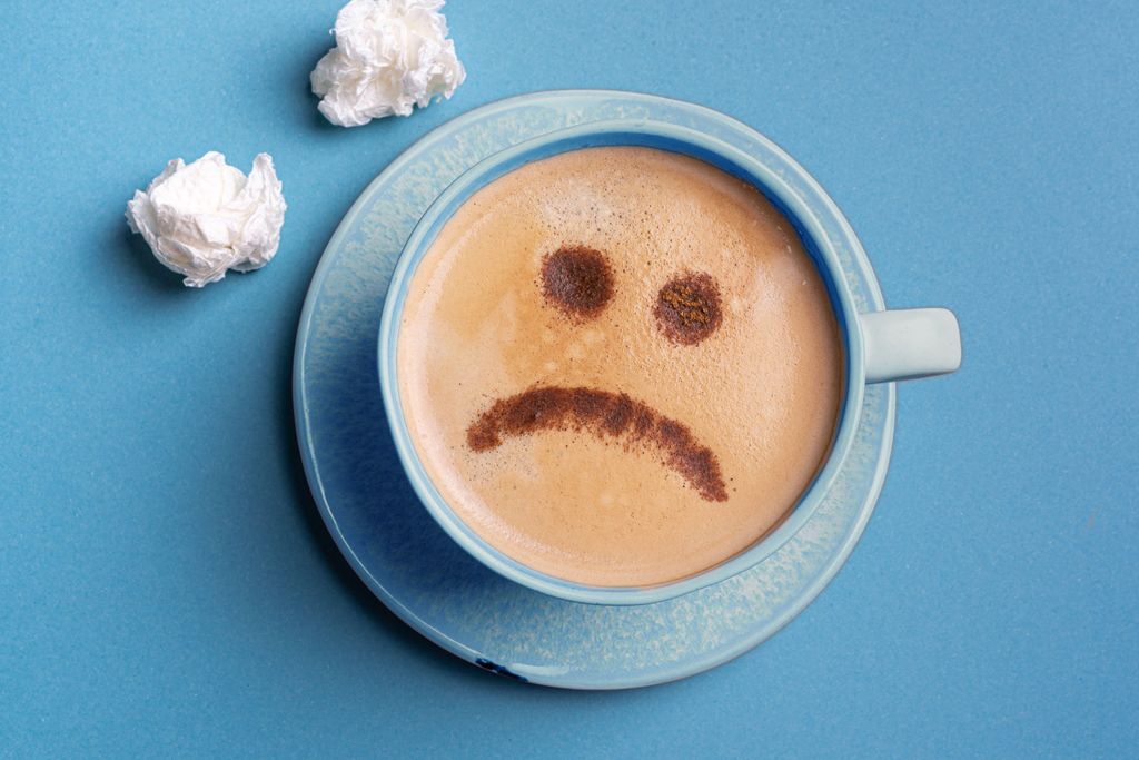 Blue Monday and depression concept. Cup of cappuccino coffee with unhappy upset sad face on blue background, top view. Seasonal disorder.