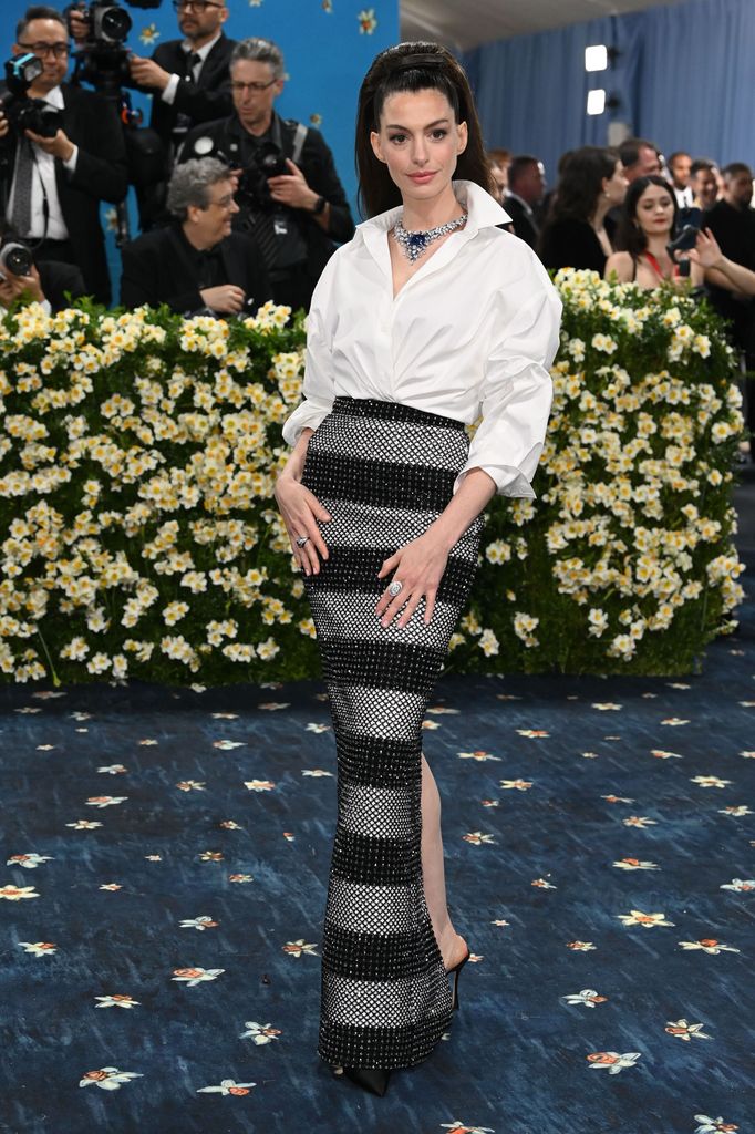 Anne Hathaway wears a white shirt and black and grey beaded striped skirt, teamed with a huge statement necklace and a 60s inspired hair do.