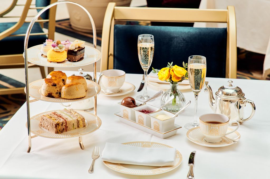 afternoon tea set on a table, with two glasses of champagne, four scones and cakes