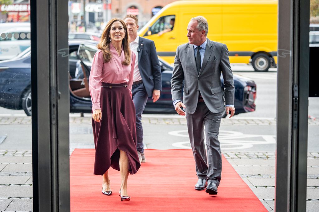 Queen Mary in burgundy heels walking with men in suits