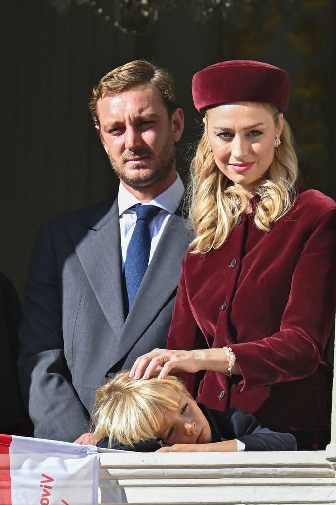 Beatrice Borromeo wears a red velvet coat and matching pillbox hat while standing beside Prince Pierre Casiraghi and their son.