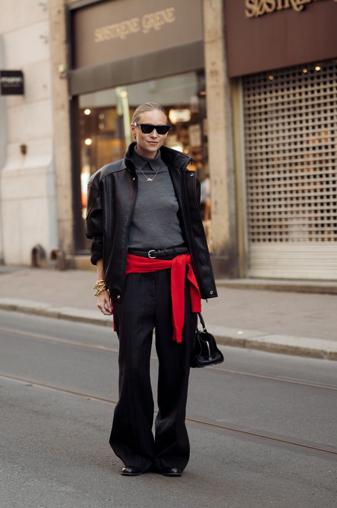 Tine Andrea wears black pants, grey top, black leather jacket, red scarf over her hips outside the Envelope 1976 show outside the Envelope 1976 show during Oslo Fashion Week