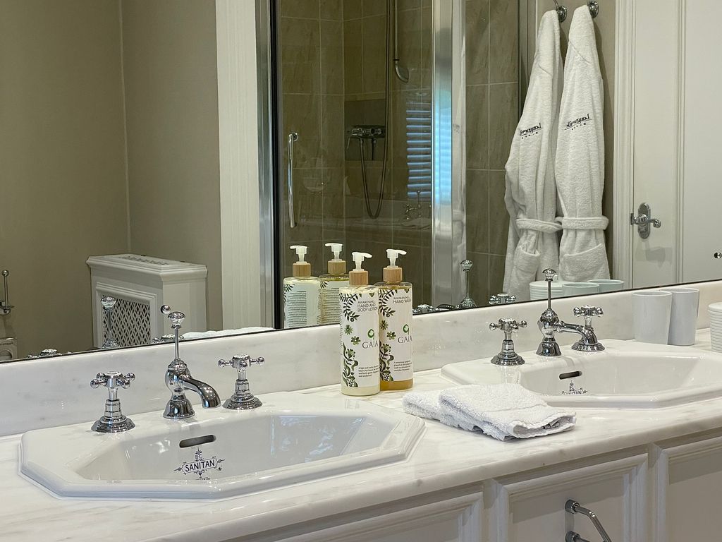 A bathroom with two sinks and mirror and two robes and a shower in the reflection