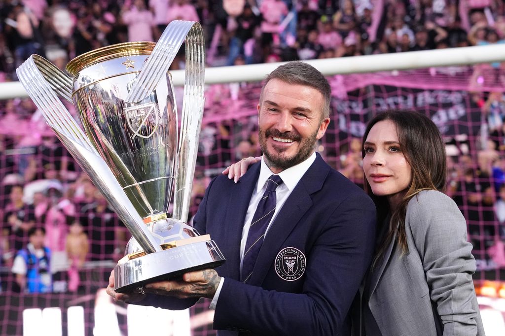 Sir David Beckham and Victoria Beckham in grey suit pose with the trophy
