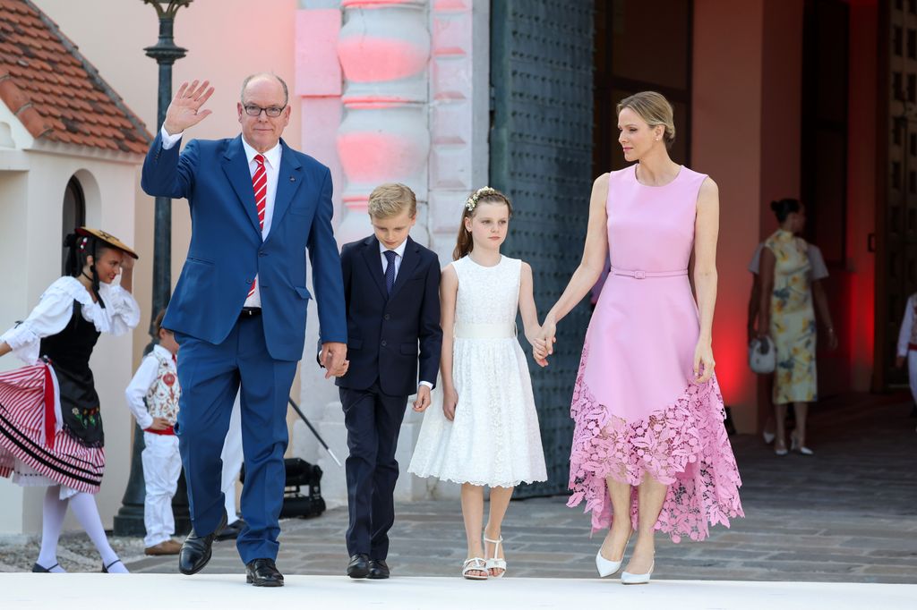 Prince Albert, Prince Jacques of Monaco in suits holding hands with Princess Gabriella in white dress and Princess Charlene in pink dress