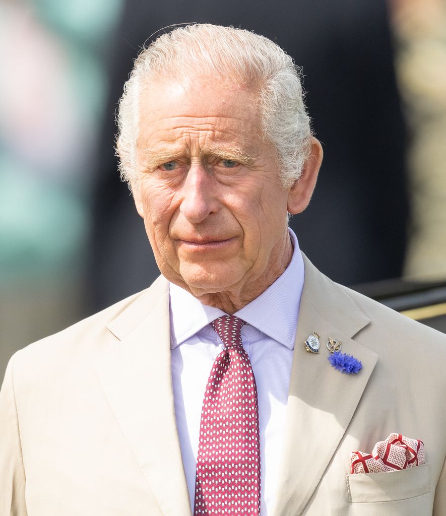 King Charles frowning in the sunshine in a cream suit