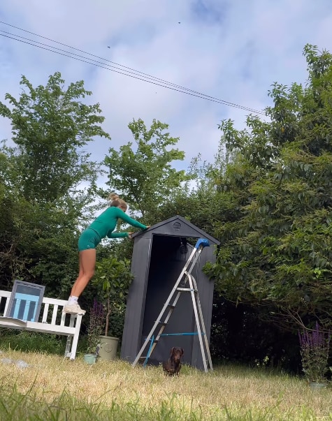 Stacey Solomon standing on a bench as she builds roof of her shed in her garden