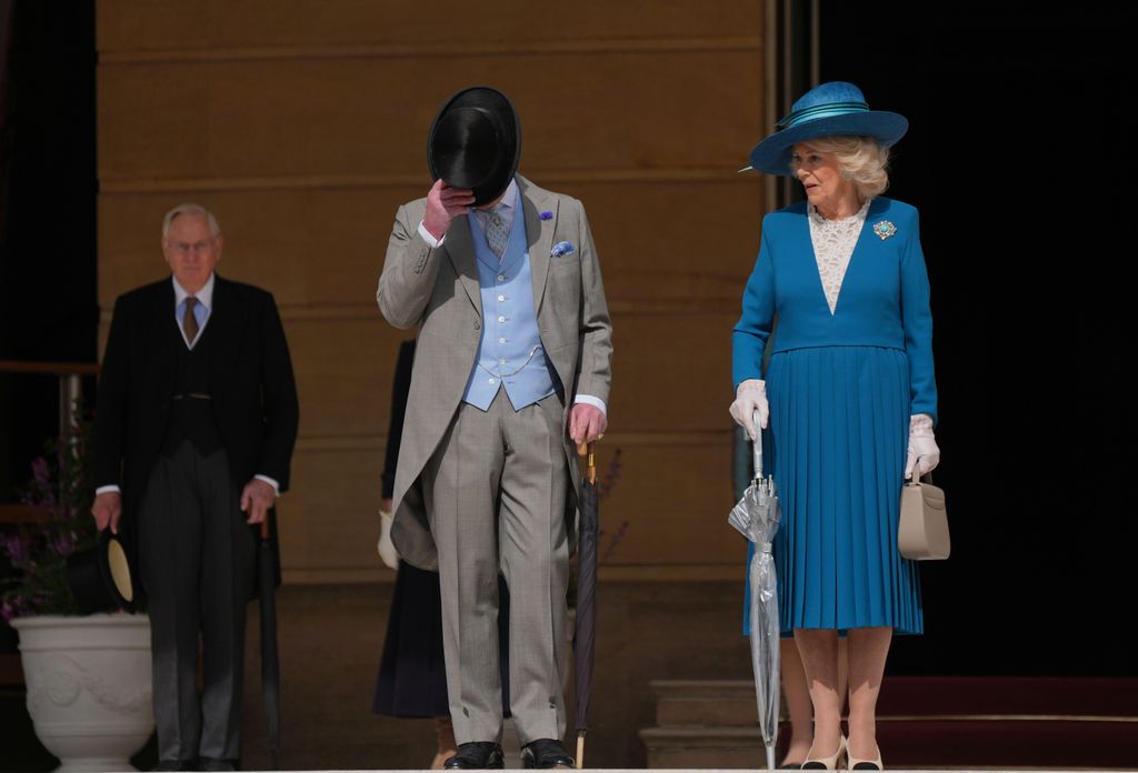 King tipping his hat and Queen Camilla in teal dress