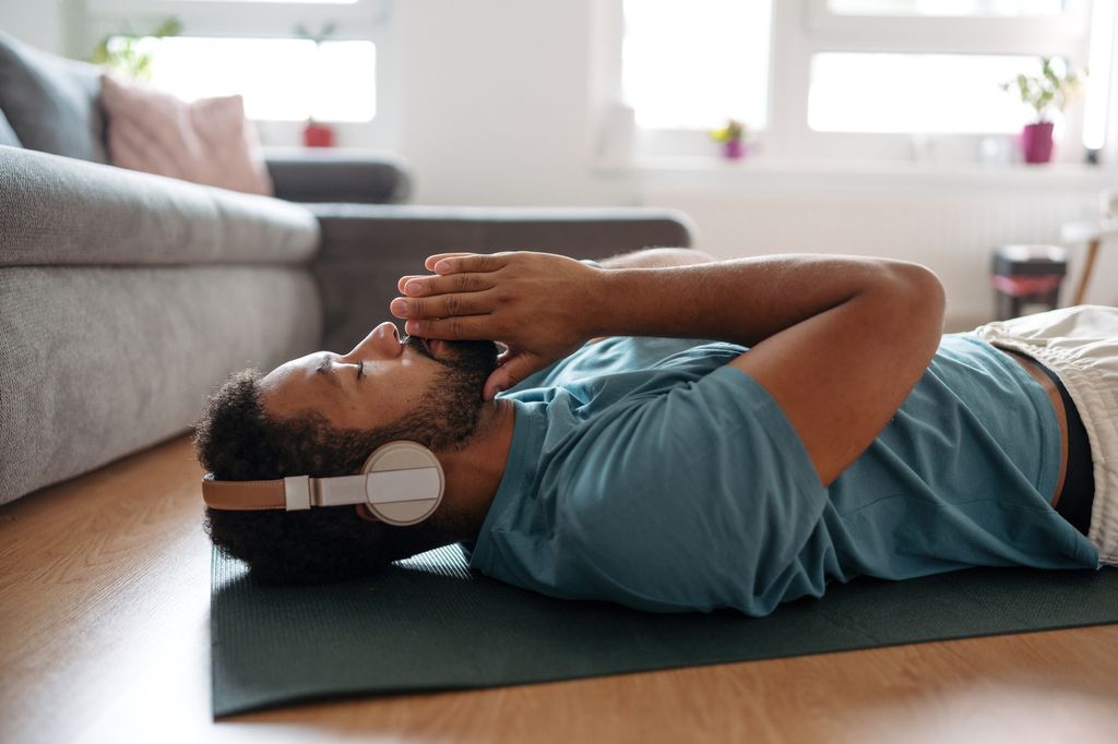 man meditating alone at home while listening to meditation music through wireless headphones, doing breathing exercises