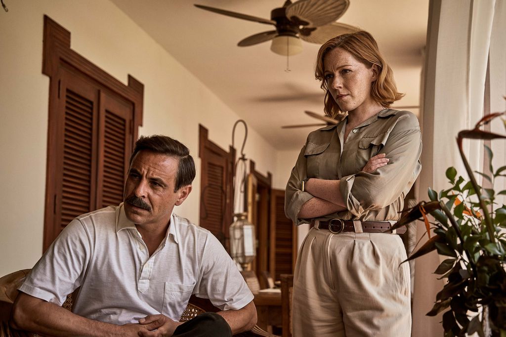 A man sitting on a chair next to a standing woman with arms folded