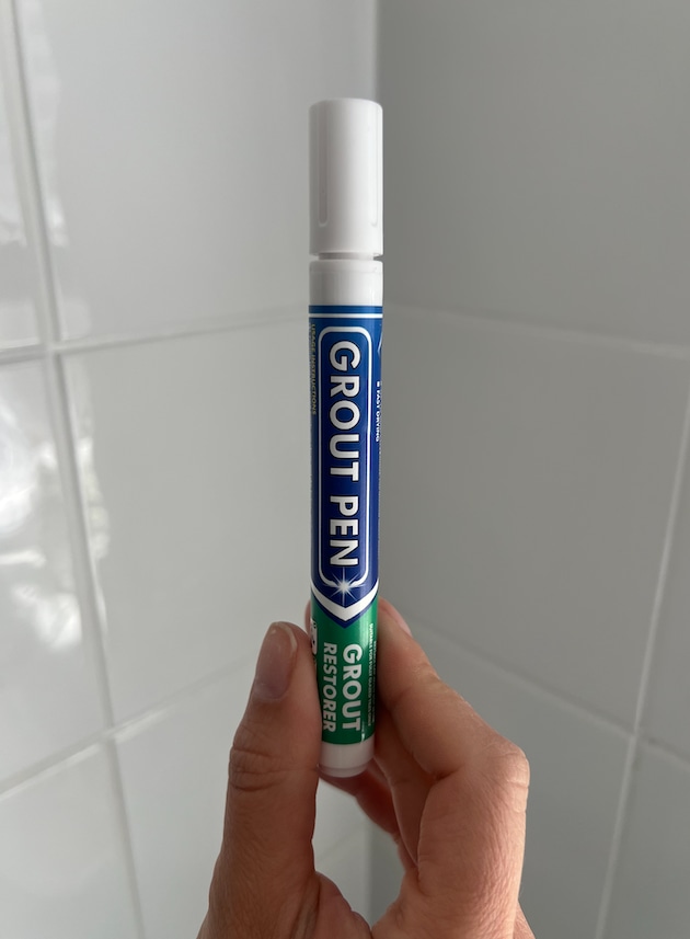 hand holding grout pen with white tiles behind