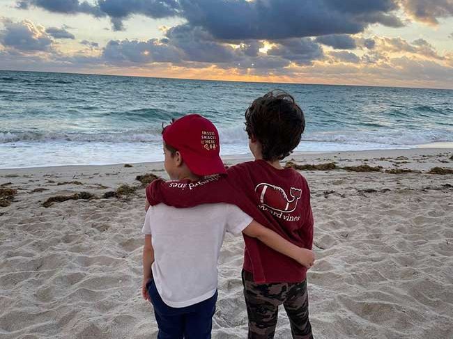 Ginger Zees sons with their backs to the camera on a beach at dusk