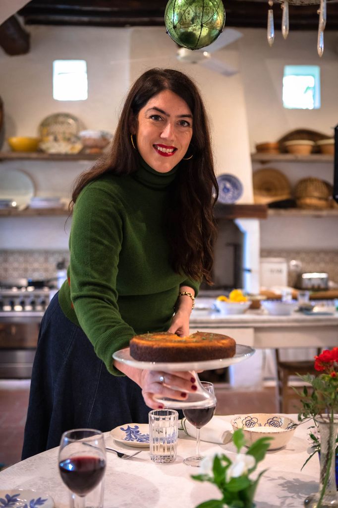 A photo of a brunette lady in a green jumper holding a cake stand