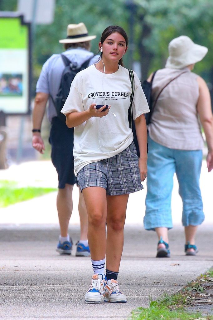 Suri Cruise, 18, stays cool in NYC wearing a cream tee, shorts, and mismatched socks while walking through Central Park.