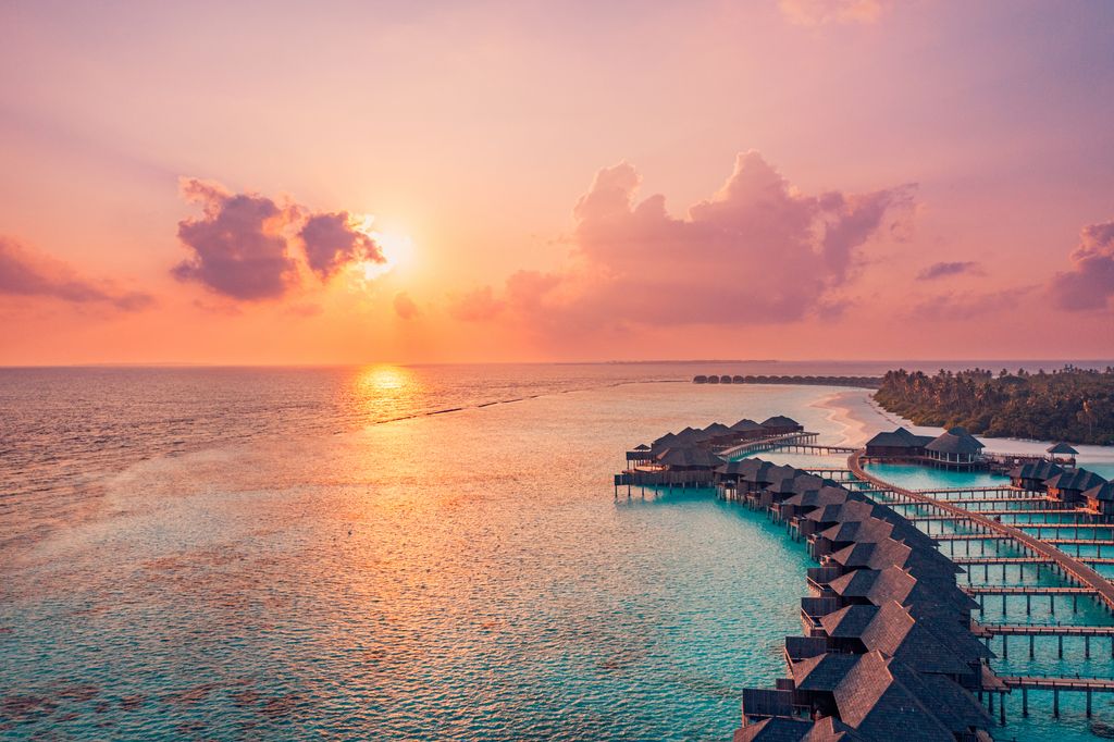 Amazing aerial beach landscape. Beautiful Maldives sunset seascape view. Horizon colorful sea sky clouds over water villa pier pathway. Tranquil drone view island lagoon tourism travel exotic vacation