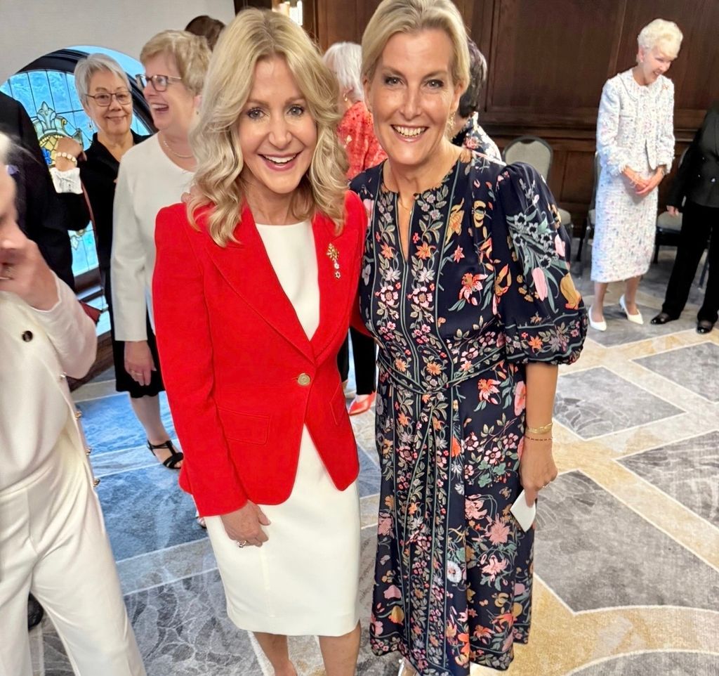 Duchess Sophie in navy floral dress posed with smiling blonde lady in white dress and red blazer