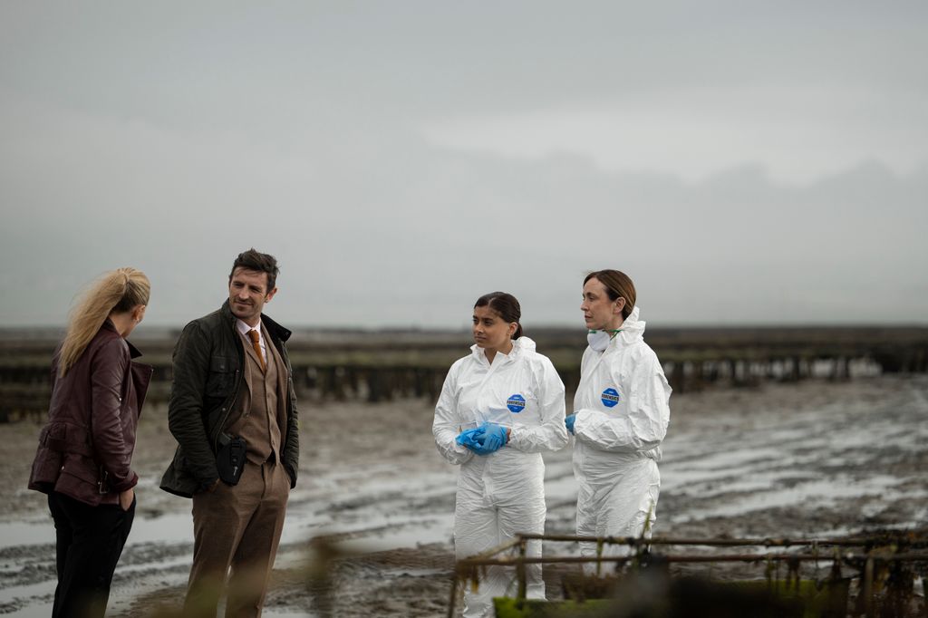two detectives standing next to two forensic scientisst on beach
